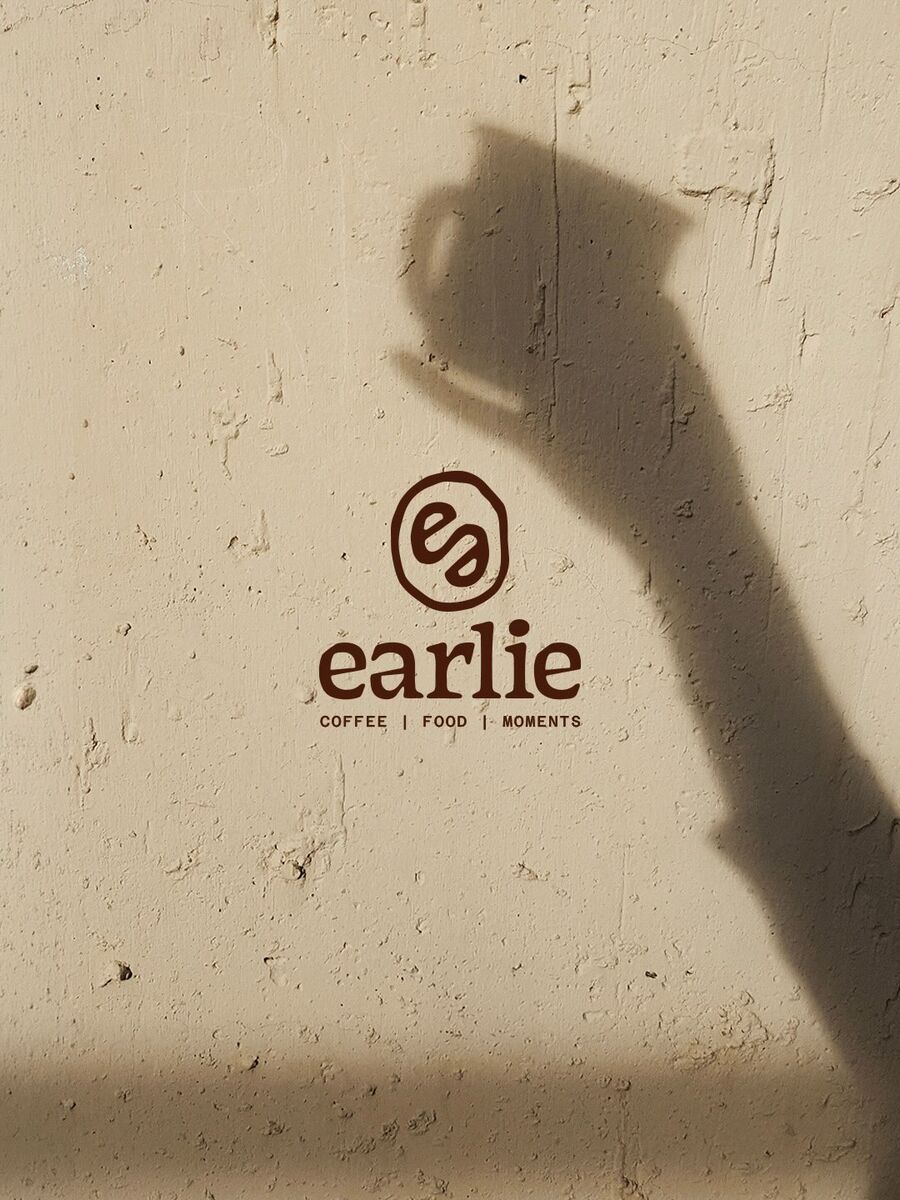 L'ombre d'une main tenant une tasse, sur un mur de pierre portant le logo Earlie.