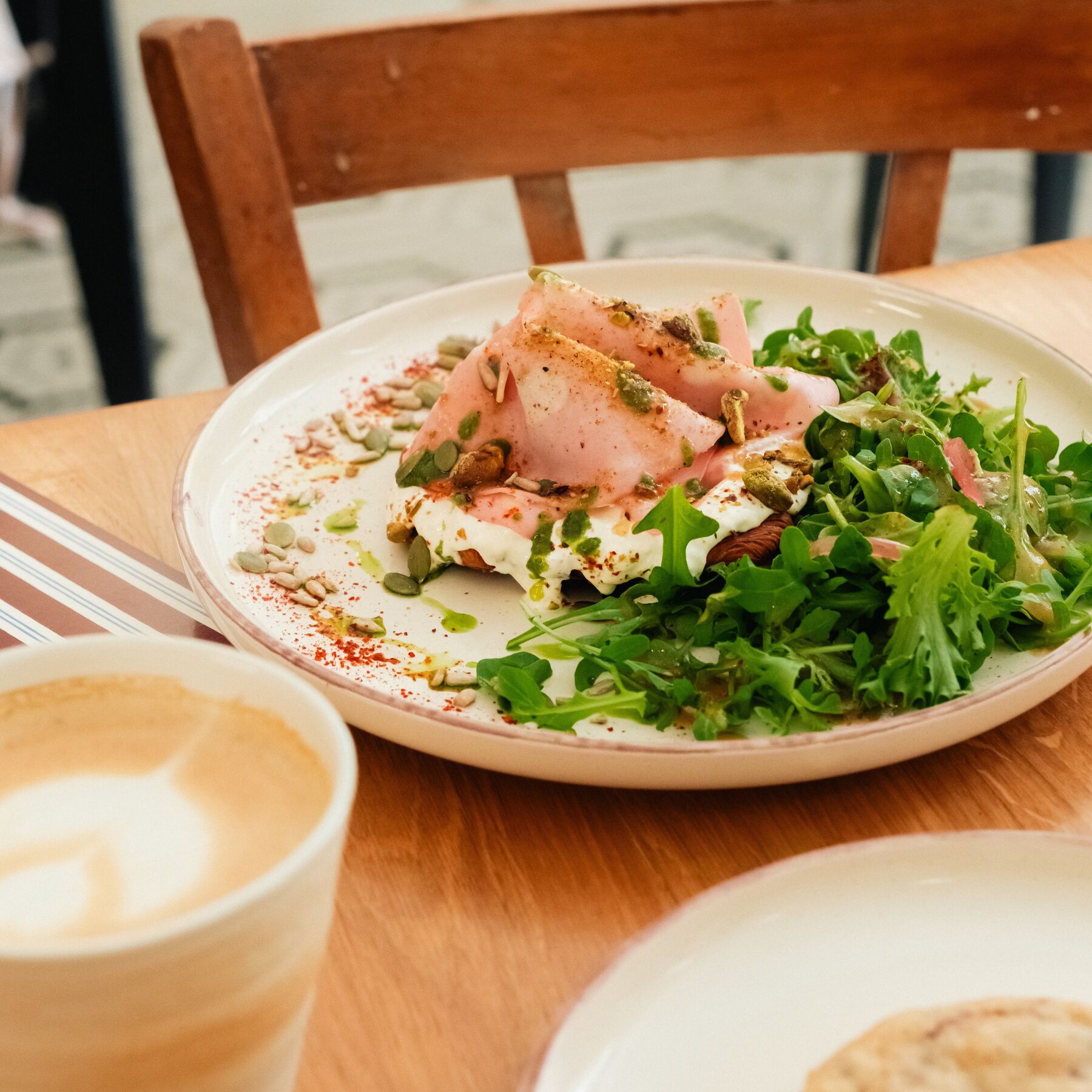Une assiette garnie de roquette et un cappuccino, sur une table en bois chez Earlie.
