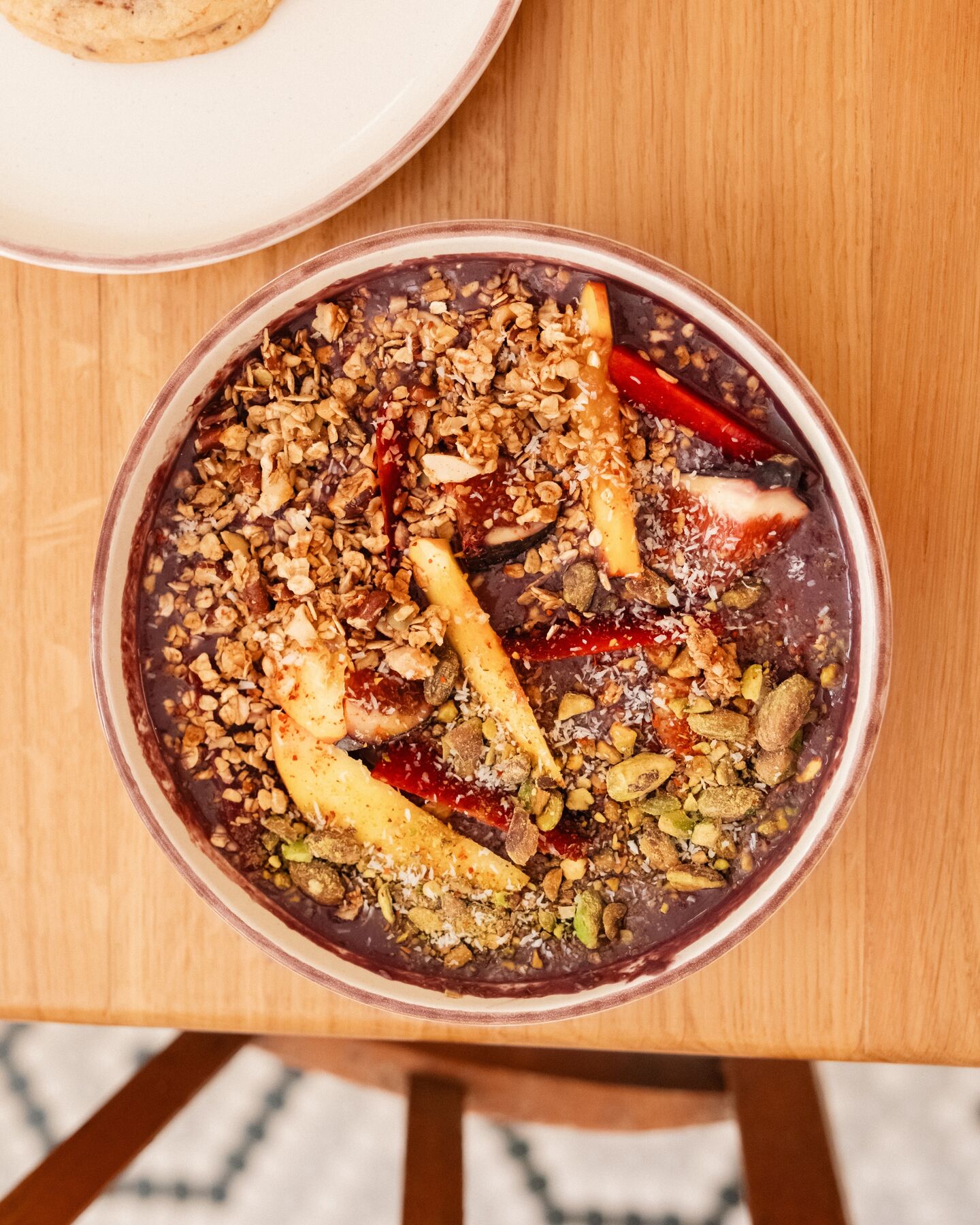 Un bowl garni de granola, de fruits et de graines, vu du dessus sur une table en bois.