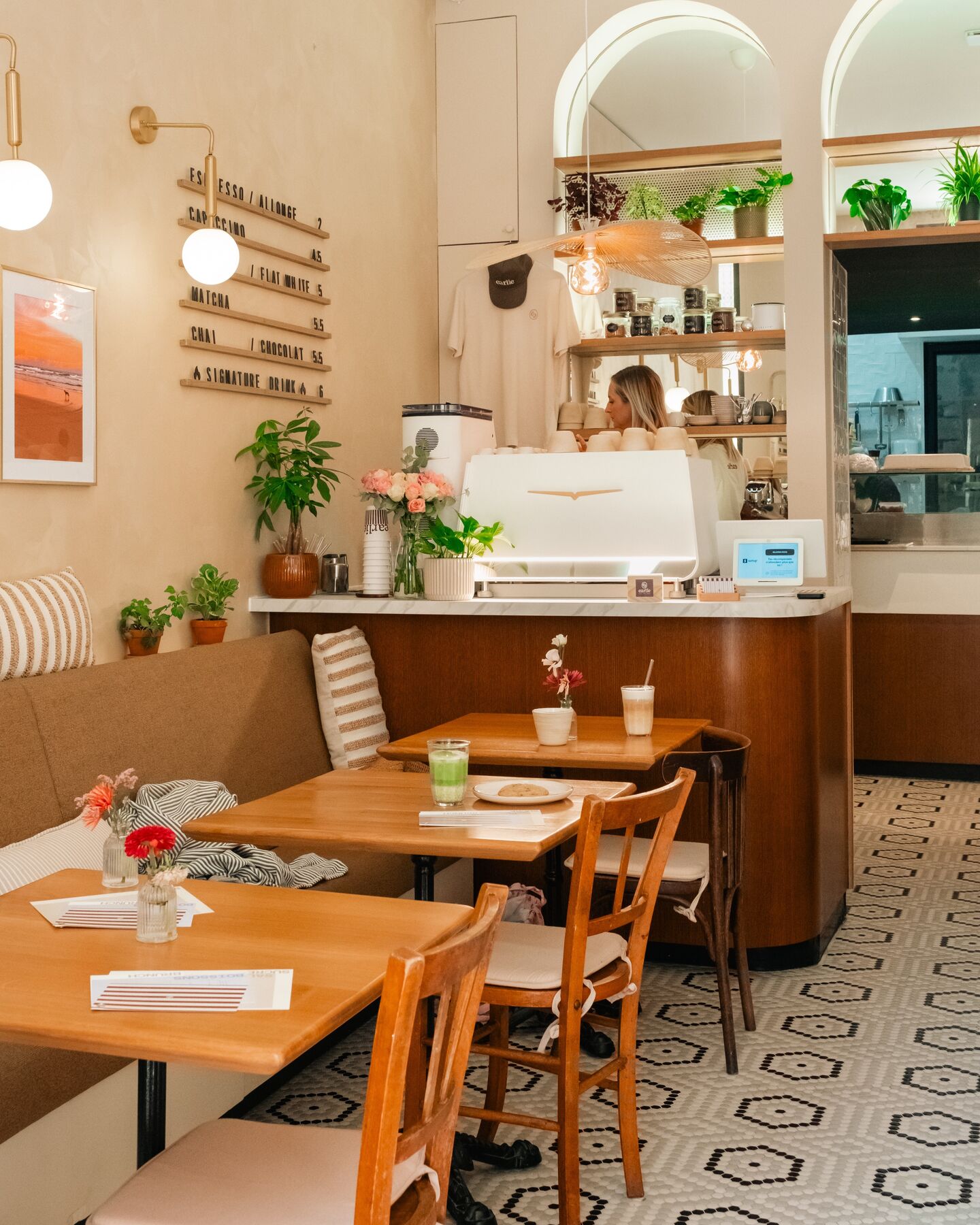 La salle d'Earlie : comptoir en bois, tables, plantes, lumière naturelle et sol à motifs.