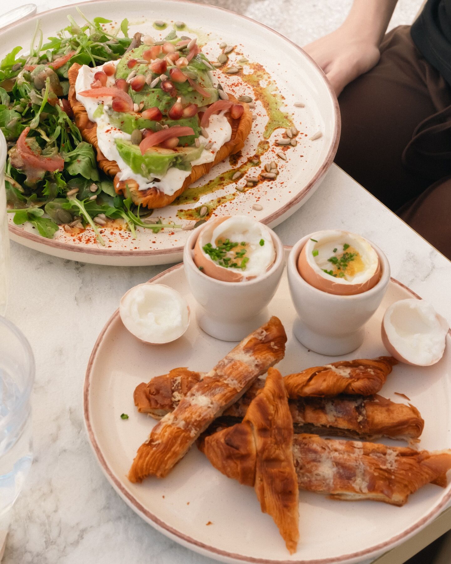 Sur une table en marbre : un croissant pressé garni, des œufs à la coque et leurs mouillettes.